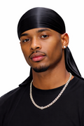 Man wearing a black durag and black shirt with a silver chain necklace on a white background